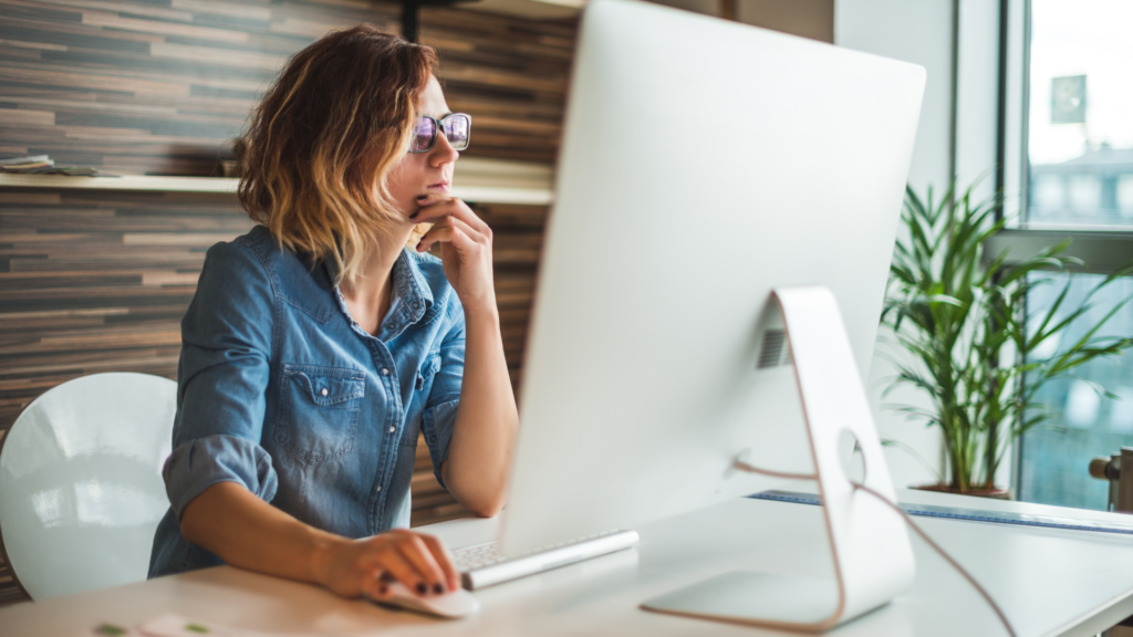 Person with blonde hair and black glasses looking at a computer desktop